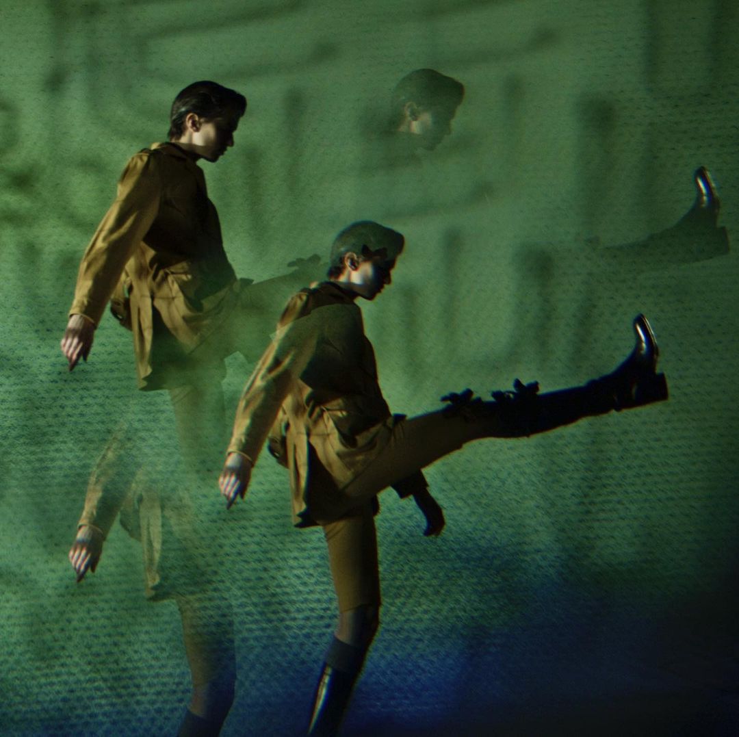 Person in a brown shirt and dark pants strikes a leg-extended pose against a green textured backdrop with multiple exposures layered together.