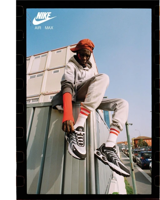 Nike Air Max campaign featuring a Black male model perched on a building, lacing up his sneaker on a sunny day in an urban setting.