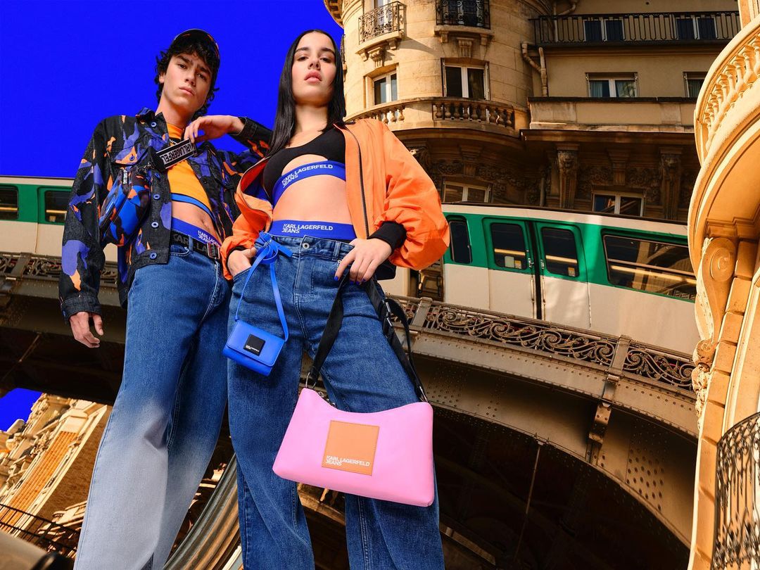 Two fashion models in Karl Lagerfeld Jeans, standing in front of Paris buildings and a metro train, showcasing contemporary style.