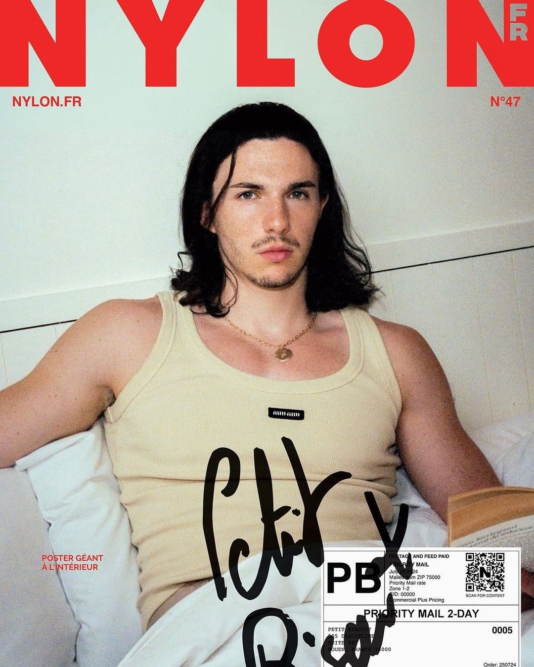 Magazine cover featuring a medium shot of a male model with long brown hair wearing a tank top, lying on a white pillow.