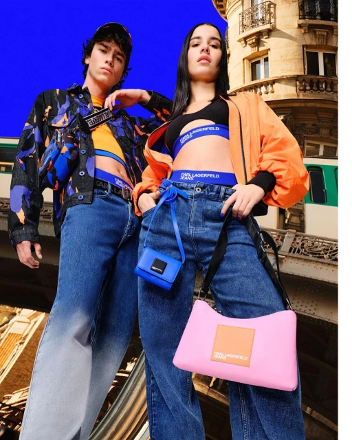 Two fashion models in Karl Lagerfeld branded apparel and accessories posing outdoors with an elevated train in the background.