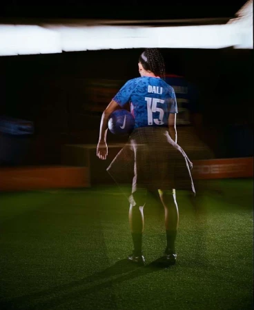 Female soccer player in a sports jersey with the number 15, holding a soccer ball, standing on a green turf field.