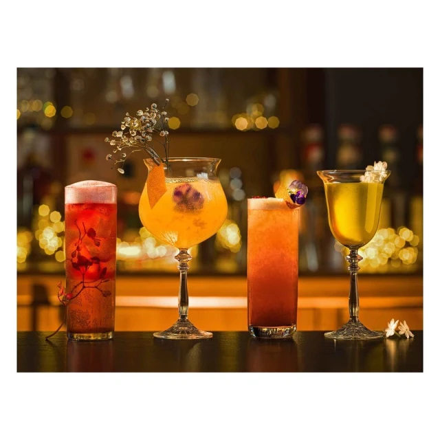 Four vibrant cocktails stand on a dark counter, illuminated by soft bokeh lighting, creating an inviting and celebratory atmosphere.