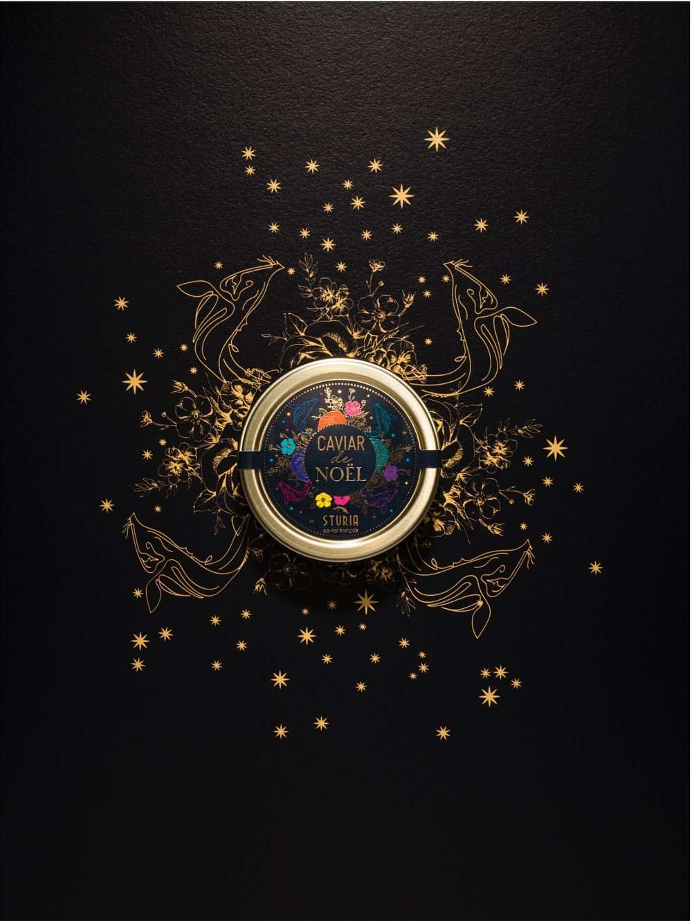 Overhead shot of a caviar tin centered on a black surface, adorned with gold stars, sketched whales, and botanical illustrations.