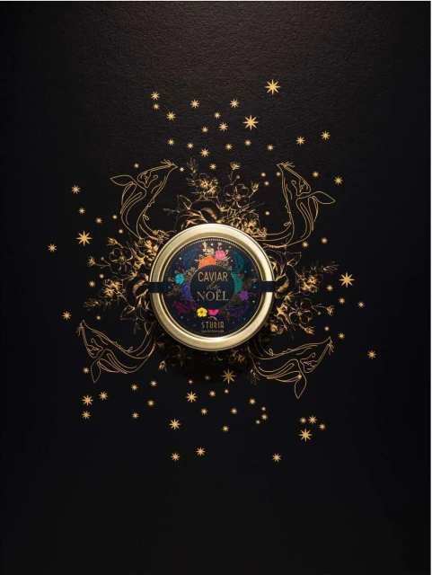 Overhead shot of a caviar tin centered on a black surface, adorned with gold stars, sketched whales, and botanical illustrations.