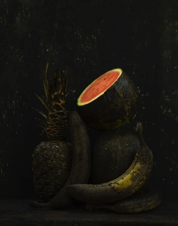 Still life photograph featuring a cut watermelon, whole pineapple, and two bananas arranged against a dark background with textured lighting.