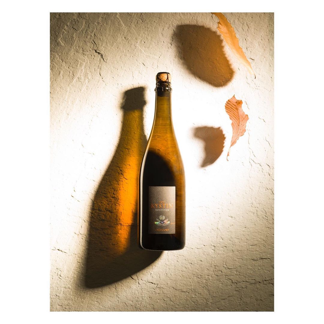 Studio shot of a cider bottle casting a long shadow, complemented by scattered autumn leaves, all set against a textured surface.