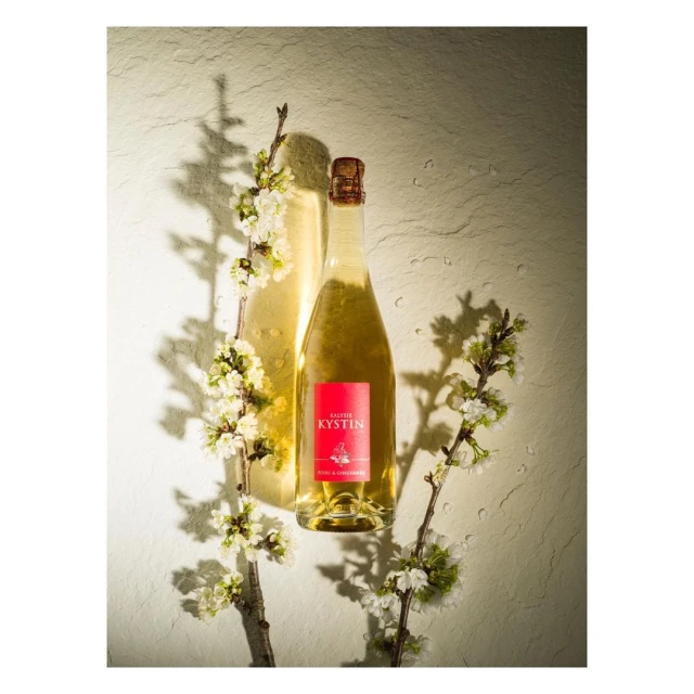 Elegant bottle of Kystin liqueur surrounded by delicate white blossoms on a textured stone background creating a visually appealing still life.