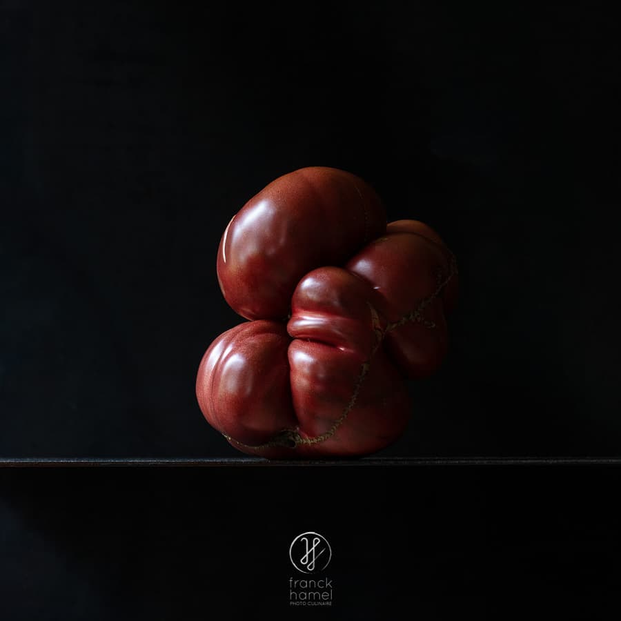 Close-up studio shot of a ripe heirloom tomato with an unusual ribbed form, isolated against a dark background. Food still life.