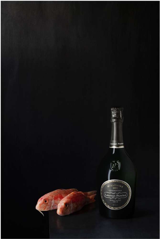 Studio shot of two red mullet fish beside a champagne bottle with black background, product photography for the food and beverage industry.