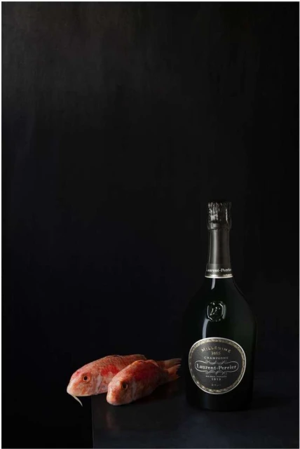 Studio shot of two red mullet fish beside a champagne bottle with black background, product photography for the food and beverage industry.
