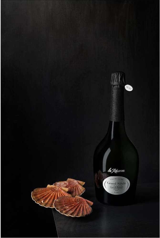 Elegant still life featuring a bottle of champagne with a black foil top, paired with four scallop shells on a dark surface.