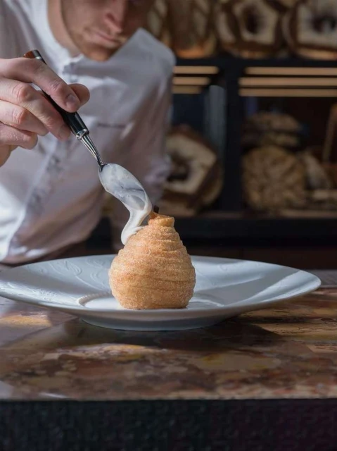 Chef garnishing dessert with cream in a restaurant, featuring a plated dessert with intricate details and a professional culinary presentation.