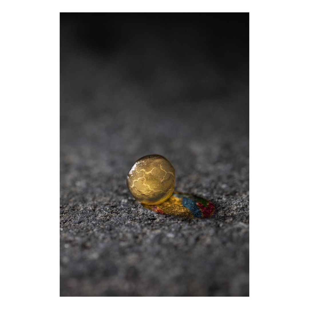 Close-up studio shot of a golden sphere with veined pattern, resting on a surface with paint streaks, against a blurred dark backdrop.