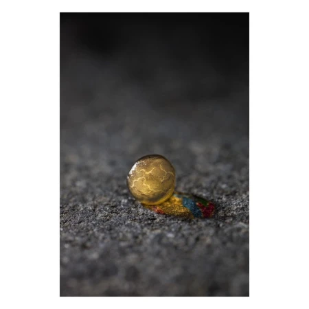 Close-up studio shot of a golden sphere with veined pattern, resting on a surface with paint streaks, against a blurred dark backdrop.