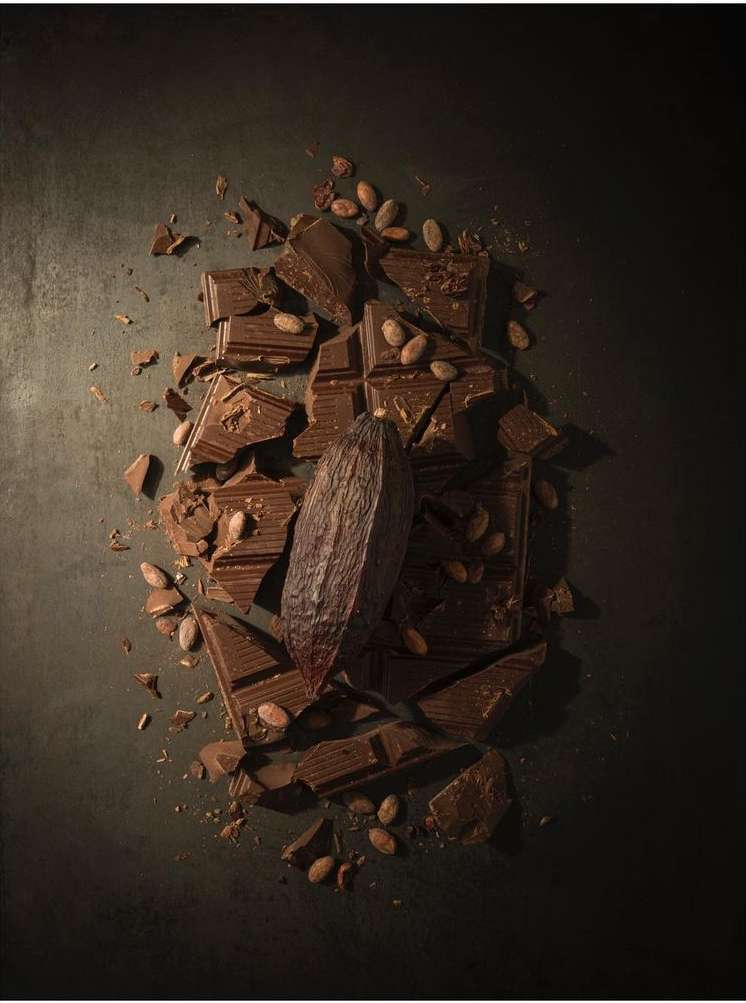 Overhead shot of dark chocolate chunks scattered with cacao beans and a single cocoa pod on a dark background, food photography.