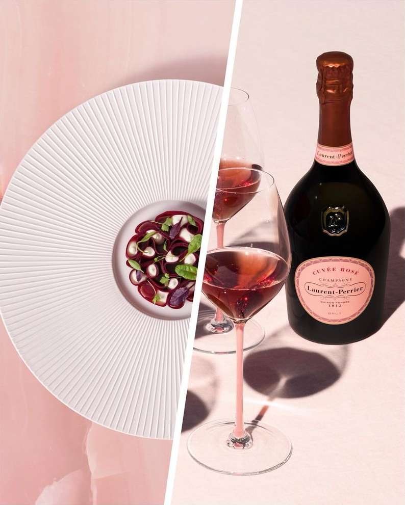 Elegant table setting featuring rose champagne in stemmed glasses alongside a plate of colorful salad on a split pink background.