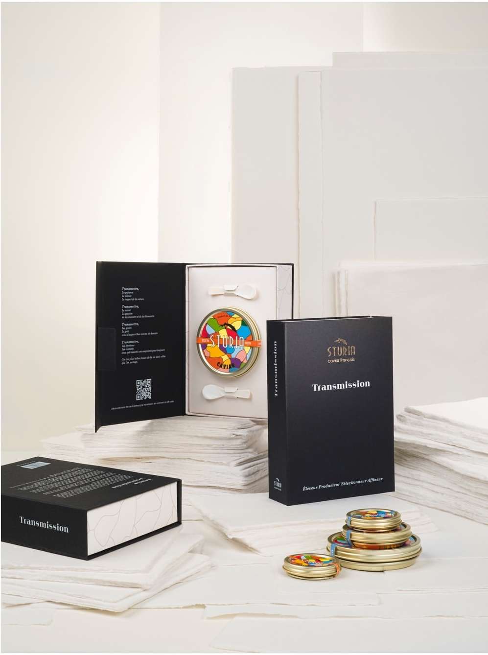 Product still life of a Sturia caviar set including tins of caviar, spoons, and product packaging, set against a white backdrop.