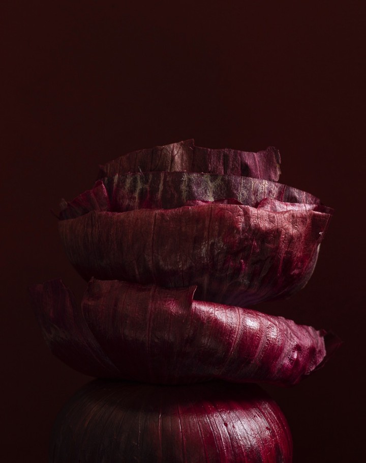 Stack of vibrant red onion halves and slices against a dark red background with dramatic lighting showcasing the vegetable's texture.