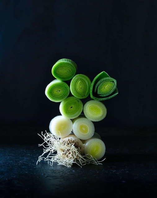 Sliced leeks stacked in a pile on a dark background, showcasing their circular shapes and green and white colors. Fresh vegetable still life.