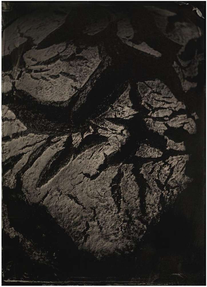Dark, moody photography showcasing the rough texture and cracks of a loaf of bread against a dimly lit background.