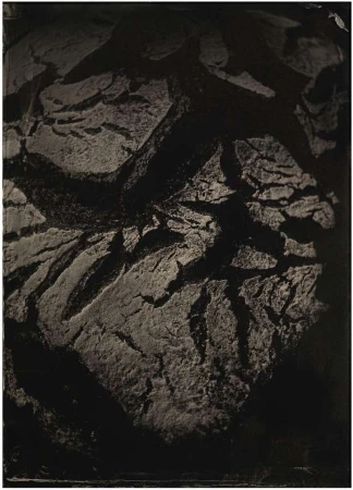 Dark, moody photography showcasing the rough texture and cracks of a loaf of bread against a dimly lit background.