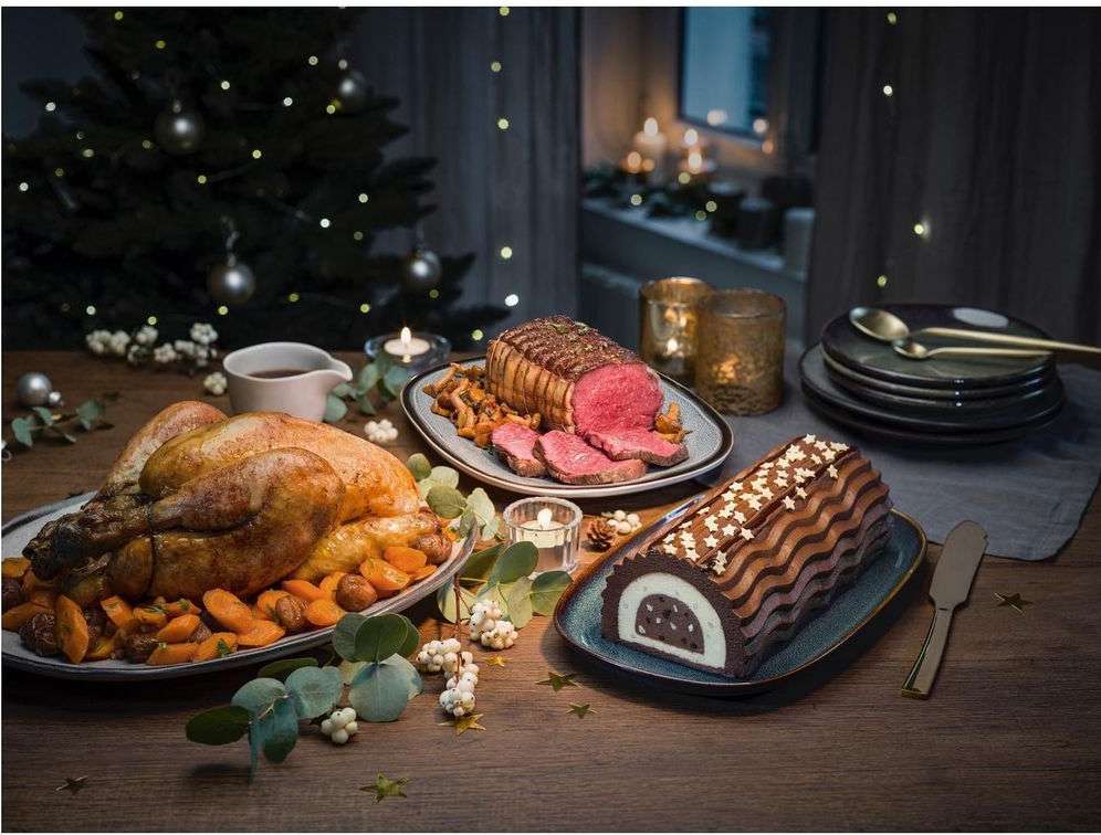 Holiday feast featuring roasted turkey, beef roast, and chocolate log cake arranged on a wooden table with festive holiday decorations.