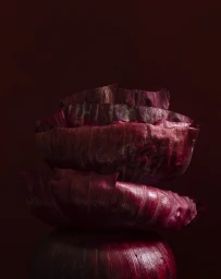 Close-up studio photograph of three stacked red cabbage sections against a dark moody background by Franck Hamel