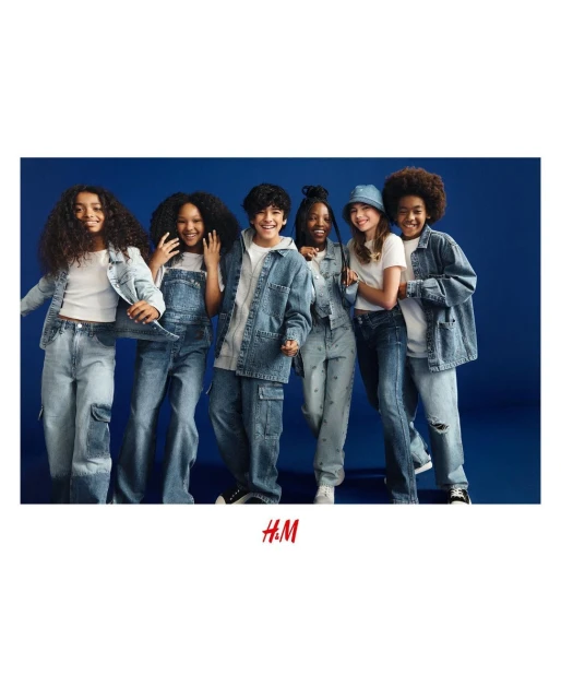 A group of five children stand in a semi-circle, all wearing denim outfits with neutral color tops against a solid dark blue backdrop.