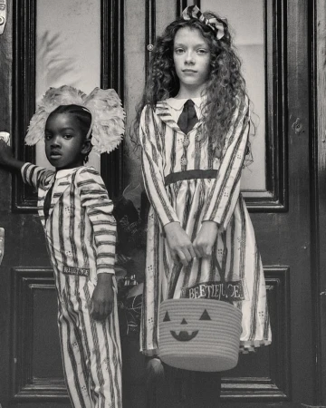 Two children in striped costumes stand in front of a door, one holding a jack-o'-lantern bucket in a grayscale photograph.