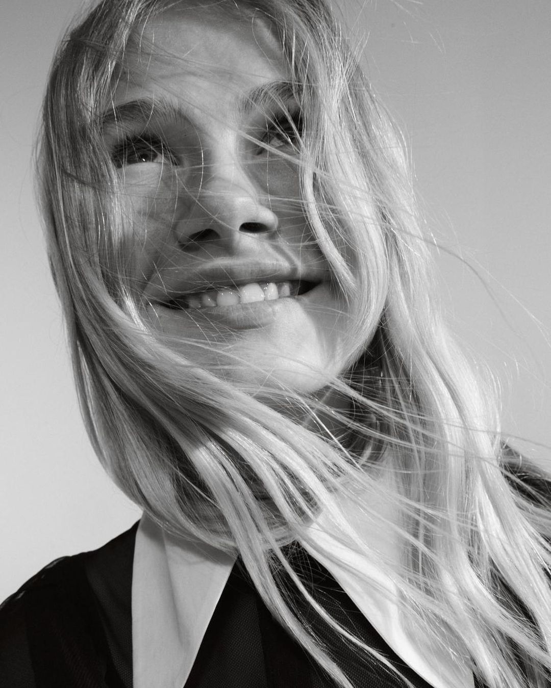 Close-up monochrome portrait of a smiling woman with long blonde hair blowing across her face in Milan, captured by Franck Malthiery.