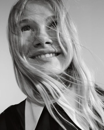 Close-up monochrome portrait of a smiling woman with long blonde hair blowing across her face in Milan, captured by Franck Malthiery.