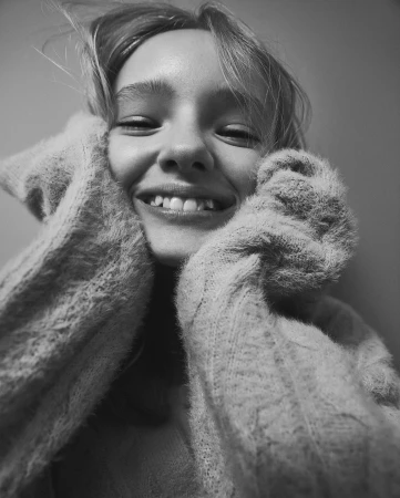 Close-up monochrome portrait of a smiling young woman holding her fuzzy knitted sweater up to her face.