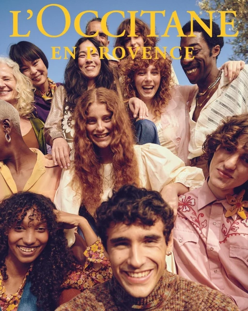 Group portrait of smiling diverse people for L'Occitane en Provence, shot at eye-level under natural lighting, against a bright blue sky.