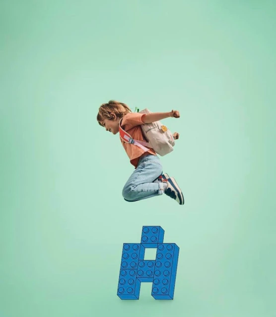 A young child with a backpack jumps over a blue building block letter 'A' against a light green backdrop in a fun, active pose.