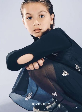 Child crouching in a dark dress with metallic embellishments against a neutral backdrop, photographed by Franck Malthiery.