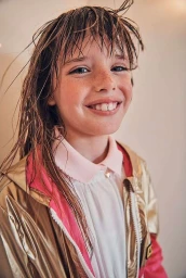 Portrait of smiling young girl with wet hair wearing a metallic gold jacket and pink collared shirt in Milan by Franck Malthiery
