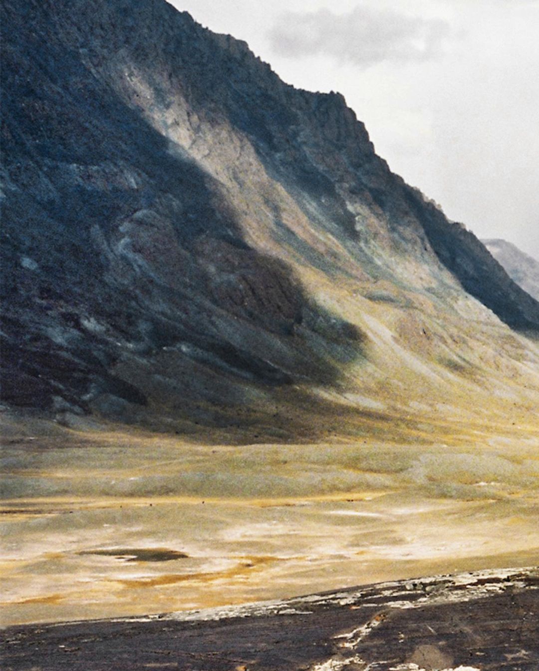 Landscape view of a large mountain range with rocky peaks and light vegetation on the lower slopes under an overcast sky.