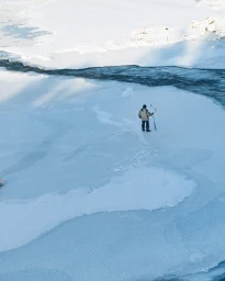 High-angle view of a person standing on a frozen snow-covered river holding an ice auger.