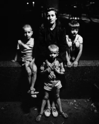 Black and white portrait of a woman seated with three children outdoors at night, photographed by Franck Pourcel in Paris