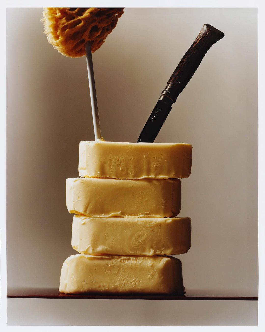 Stack of artisanal soaps with natural sponge and knife. Ivory color palette with soft lighting. Beauty product photography.