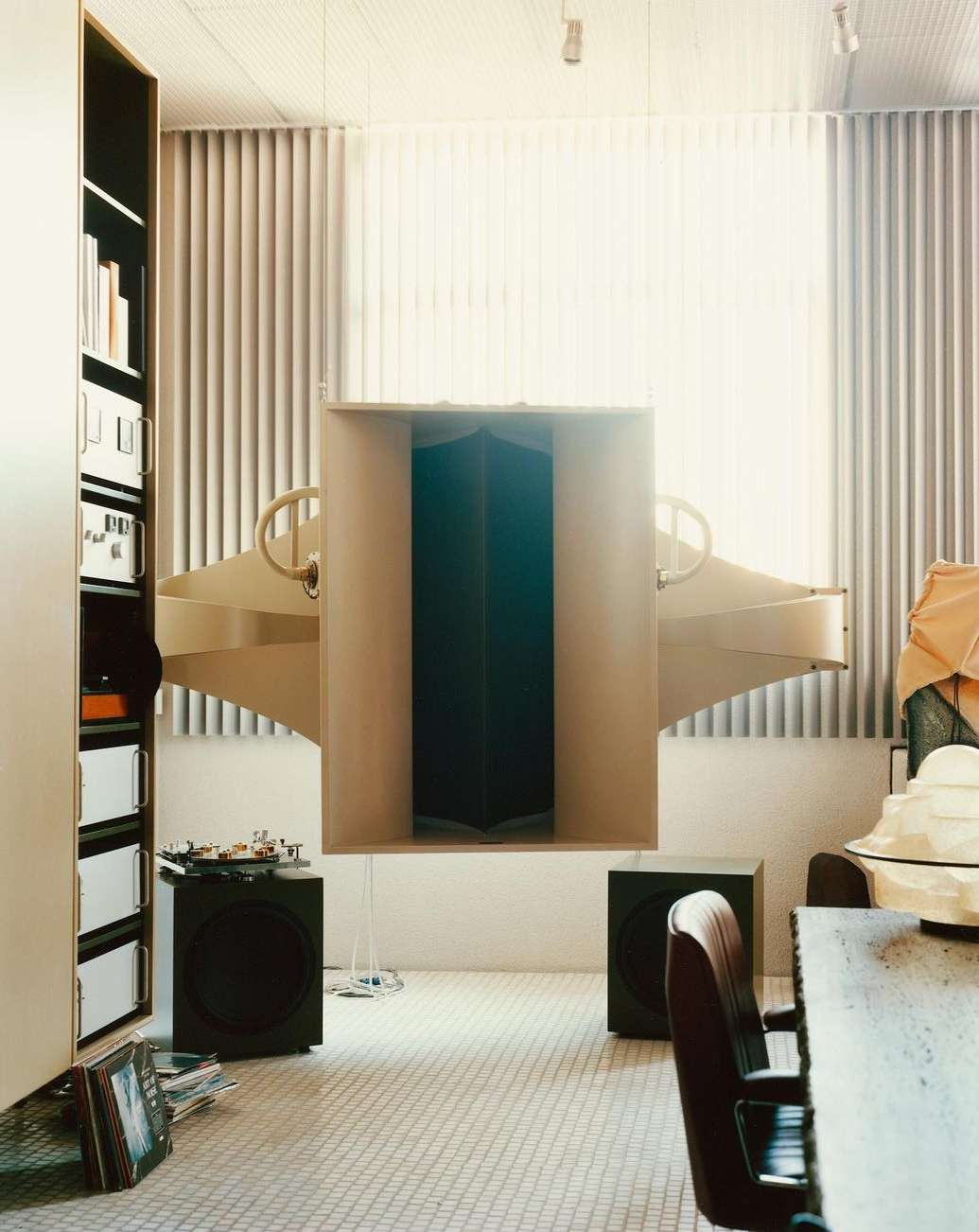 Living room interior featuring large horn speakers, black subwoofers, modern furniture, built-in shelving, and a textured floor. 