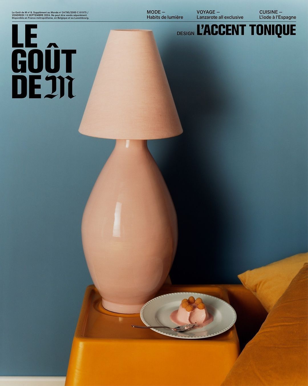 Still life of a pink table lamp, a small white plate with dessert, and an orange side table against a blue wall, creating a modern interior.