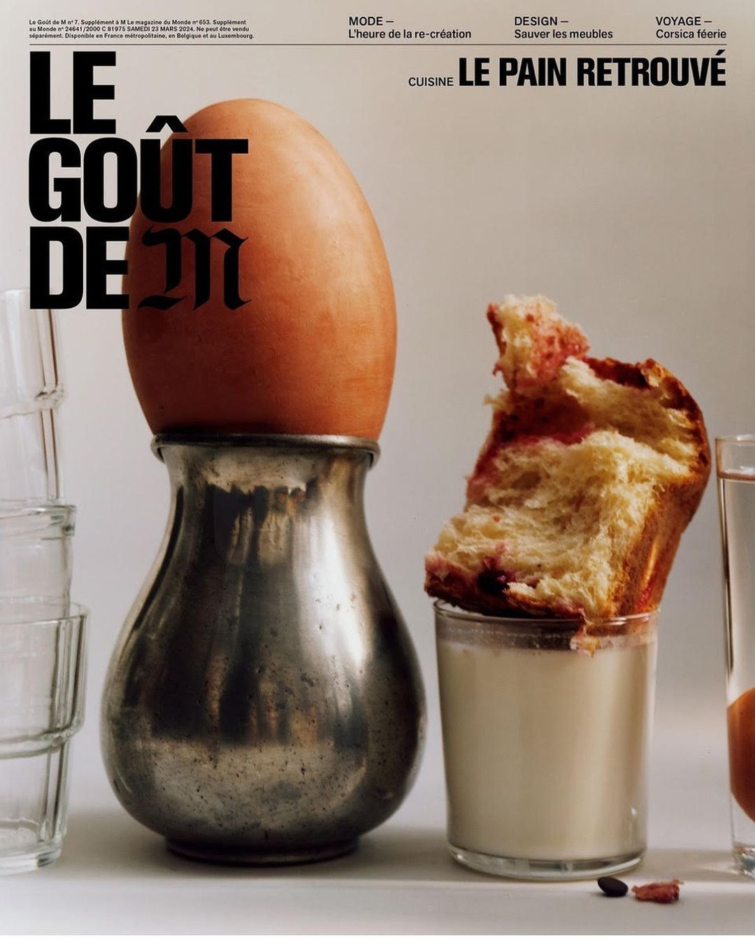 Magazine cover showcases an egg atop an ornate silver egg cup, bread, and a glass of water, set against a minimalist white background.