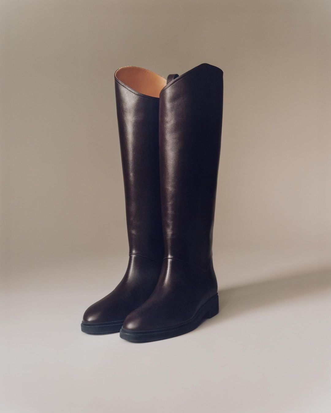 Pair of dark brown leather knee-high boots on a neutral surface, showcasing texture, design, and classic footwear style.
