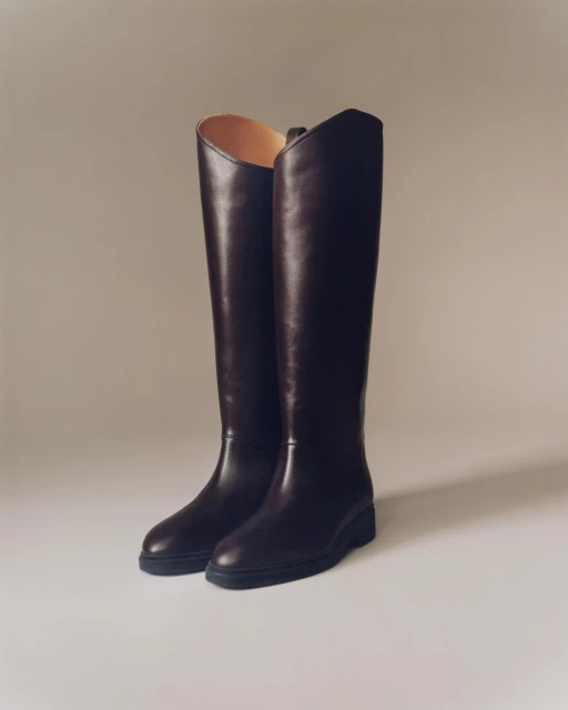 Pair of dark brown leather knee-high boots on a neutral surface, showcasing texture, design, and classic footwear style.