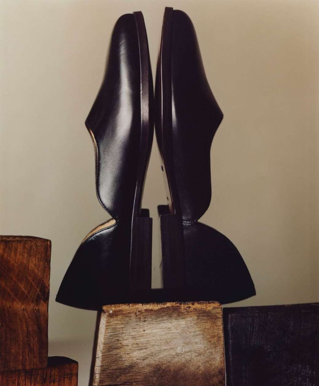 High-fashion photography features two black heeled shoes arranged on wooden blocks against a cream backdrop in a studio setting.