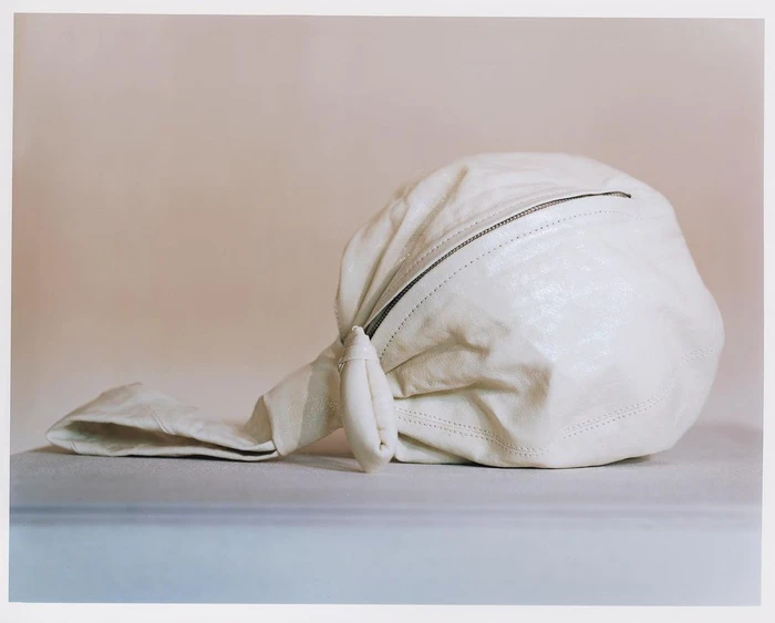 Close-up product photograph of a white leather handbag with a knotted strap and zipper against a neutral studio backdrop.