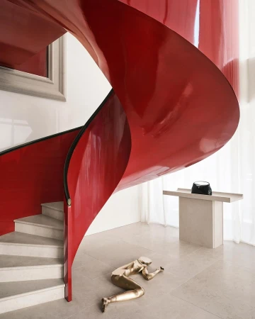 Interior view of a modern residence featuring a red spiral staircase, a golden statue, and a minimalist console table in a bright room.