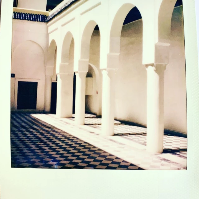Architectural view of an interior courtyard featuring a black and white checkered floor, white pillars, and arched entryways in a clean, linear design.
